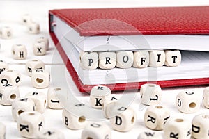 Word Profit written in wooden blocks in red notebook on white wooden table.