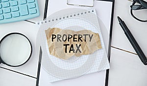 Word Property Tax is written in a notebook lying on a black table with a pen, glasses and a calculator