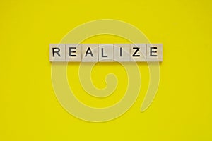 Word realize. Top view of wooden blocks with letters on yellow surface