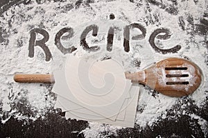 Word recipe written in white flour and spatula on wood