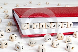 Word Refinance written in wooden blocks in red notebook on white wooden table photo
