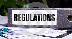 The word REGULATIONS is written on a gray file folder next to documents. Business concept photo