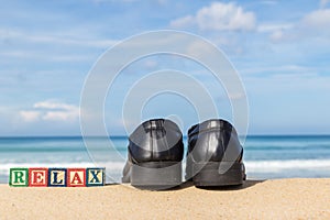 word RELAX in colorful alphabet blocks and black shoe on tropical beach