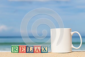 word RELAX in colorful alphabet blocks and coffee cup on tropical beach