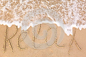 Word `RELAX` written on sandy beach and sea wave