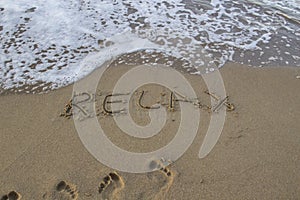 Word RELAX wrote on the sand against background. Message says