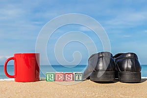 Word REST in colorful alphabet blocks and coffee cup on tropical