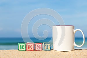 Word REST in colorful alphabet blocks and coffee cup on tropical