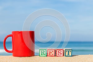Word REST in colorful alphabet blocks and coffee cup on tropical