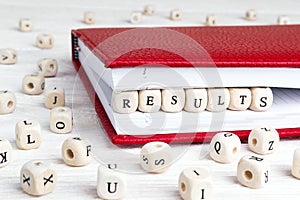 Word Results written in wooden blocks in red notebook on white w