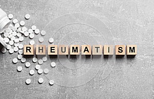 Word Rheumatism made of cubes and pills on light gray textured background, flat lay