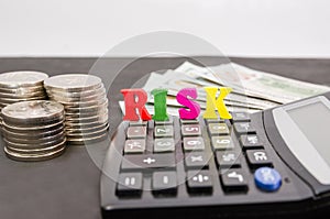 The word `risk` is folded with letters / calculator / stacks of coins and dollars. Close-up. The concept of business risk, economi