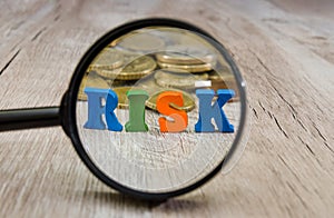 The word `risk` laid out of letters through a magnifying glass / coins on a wooden background. The concept of economic risk.