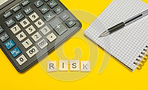 Word risk made with wood letters on yellow background and modern calculator with pen and notebook. Copy space. Economy, money