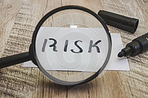The word `risk` through a magnifier, written in black marker. Close-up. Wood background.