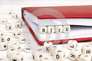 Word Risk written in wooden blocks in red notebook on white wood