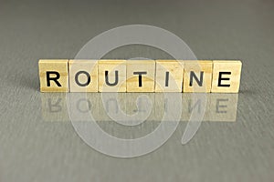 Word routine is made up of square wooden letters on a gray background