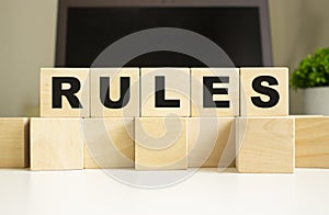 The word RULES is written on wooden cubes lying on the office table in front of a laptop.