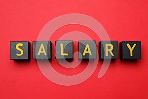Word Salary made with black wooden cubes on red background, flat lay