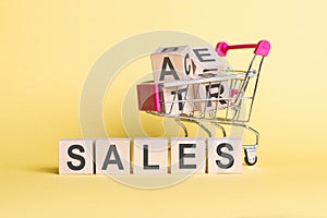 The word SALES on wooden cubes, on a yellow background with a shopping trolley