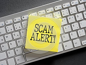The word scam alert written on a sticky note paper on computer keyboard. Scam warning or fraud notice