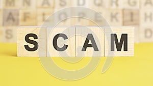 Word scam is written on wooden cubes on a bright yellow surface, concept