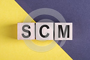 Word SCM - Supply Chain Management, on wooden cubes on yellow - gray background