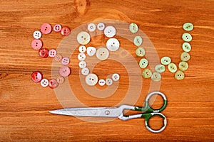 Word sew from multicolored sewing buttons and scissors on wooden background