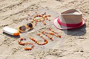 Word and shape of sun, sunglasses, sun lotion and straw hat on sand at beach, summer time concept