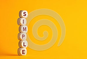 The word simple on wooden cubes against yellow background. Simplicity principle in life, business or education
