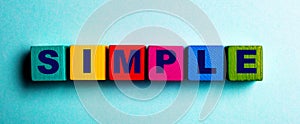 The word SIMPLE is written on multicolored bright wooden cubes on a light blue background