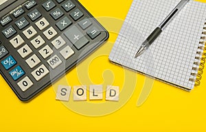 Word sold made with wood letters on yellow background and modern calculator with pen and notebook. Copy space. Economy, money