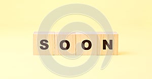 Word soon with letters on small wooden blocks on yellow