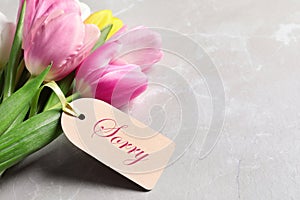 Word Sorry written on label and bouquet of tulips on light grey marble table, closeup. Space for text