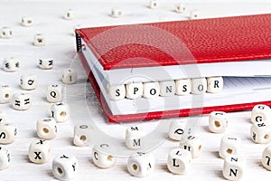 Word Sponsor written in wooden blocks in red notebook on white w