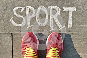 Word sport written on gray pavement with woman legs in sneakers, view from above