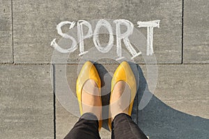 Word sport written on gray pavement with woman legs, view from above