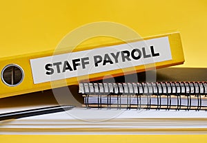 The word staff payroll written on the label of a yellow binder on the office desk