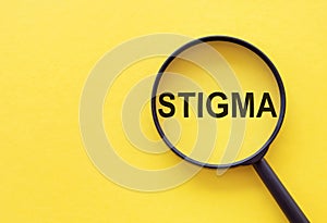 The word STIGMA is written on a magnifying glass on a yellow background