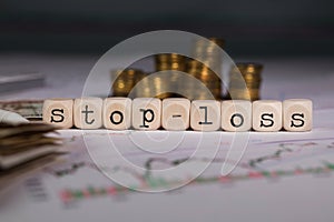 Word STOP-LOSS composed of wooden letter. Stacks of coins in the background photo