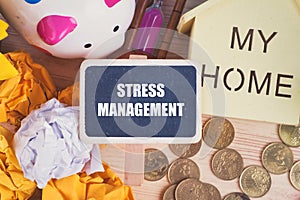 Word STRESS MANAGEMENT on wooden signage over crumple paper, piggy bank  and coins background