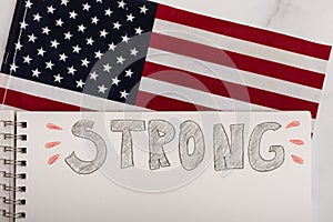 The word strong hand written on white paper American stars and stripes flag in the background