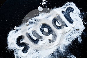 Word sugar of white granulated sugar and powdered sugar on dark stone background, top view