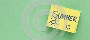 The word SUMMER on a small piece of paper and a green background. Time for rest and summer vacation