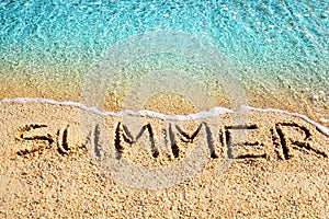 Word SUMMER written on yellow sand, blue sea water wave, white foam top view close up, handwriting letters text, summer vacations