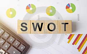 The word SWOT on wooden cubes on colorful diagram chart with calculator, top view, flatly