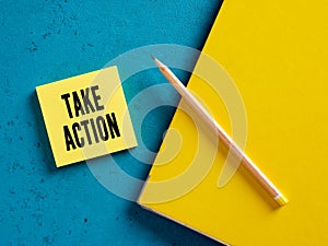 The word take action on yellow sticky note paper with a pencil and binder