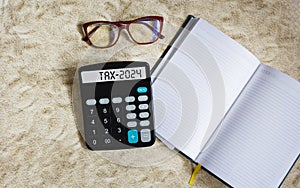 The word Tax 2024 on a calculator. Business and taxation concept. Calculator, book, glasses on the table