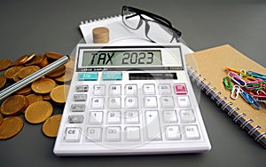 Word Tax 2023 on the calculator. Business and tax concept .Calculator, currency, book, tax form, and pen on gray desk table.