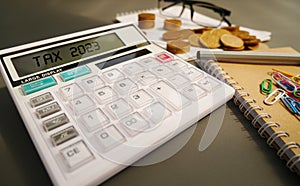 Word Tax 2023 on the calculator. Business and tax concept .Calculator, currency, book, tax form, and pen on gray desk table.